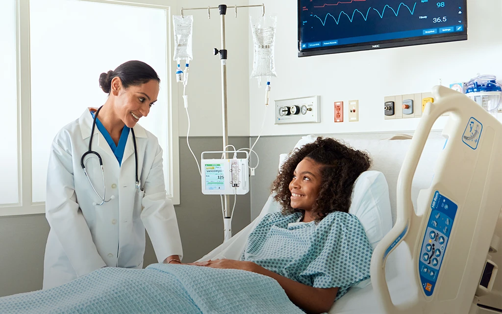 Krankenhauspersonal und Patientin am Krankenhausbett lächeln sich gegenseitig an