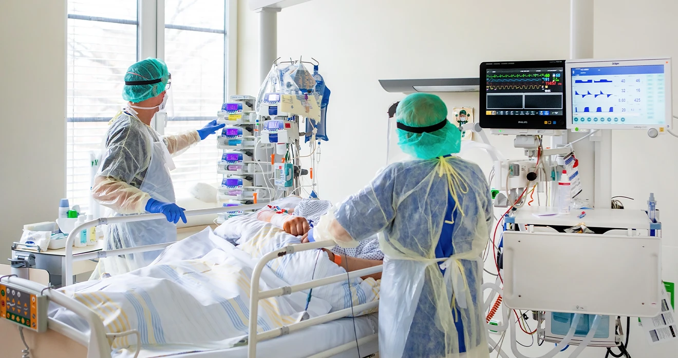 Zwei Personen des Medizinpersonals stehen neben einem Patienten oder einer Patientin und beobachten oder behandeln diese:n.