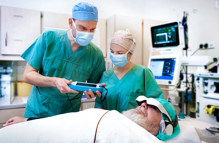 Zwei Personen des Medizinpersonals untersuchen oder behandeln einen liegenden Patienten mit einem Gerät.