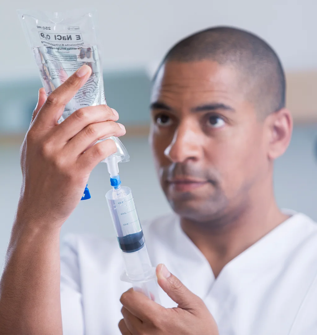 A healthcare worker filling a syringe with a liquid from a medical bag