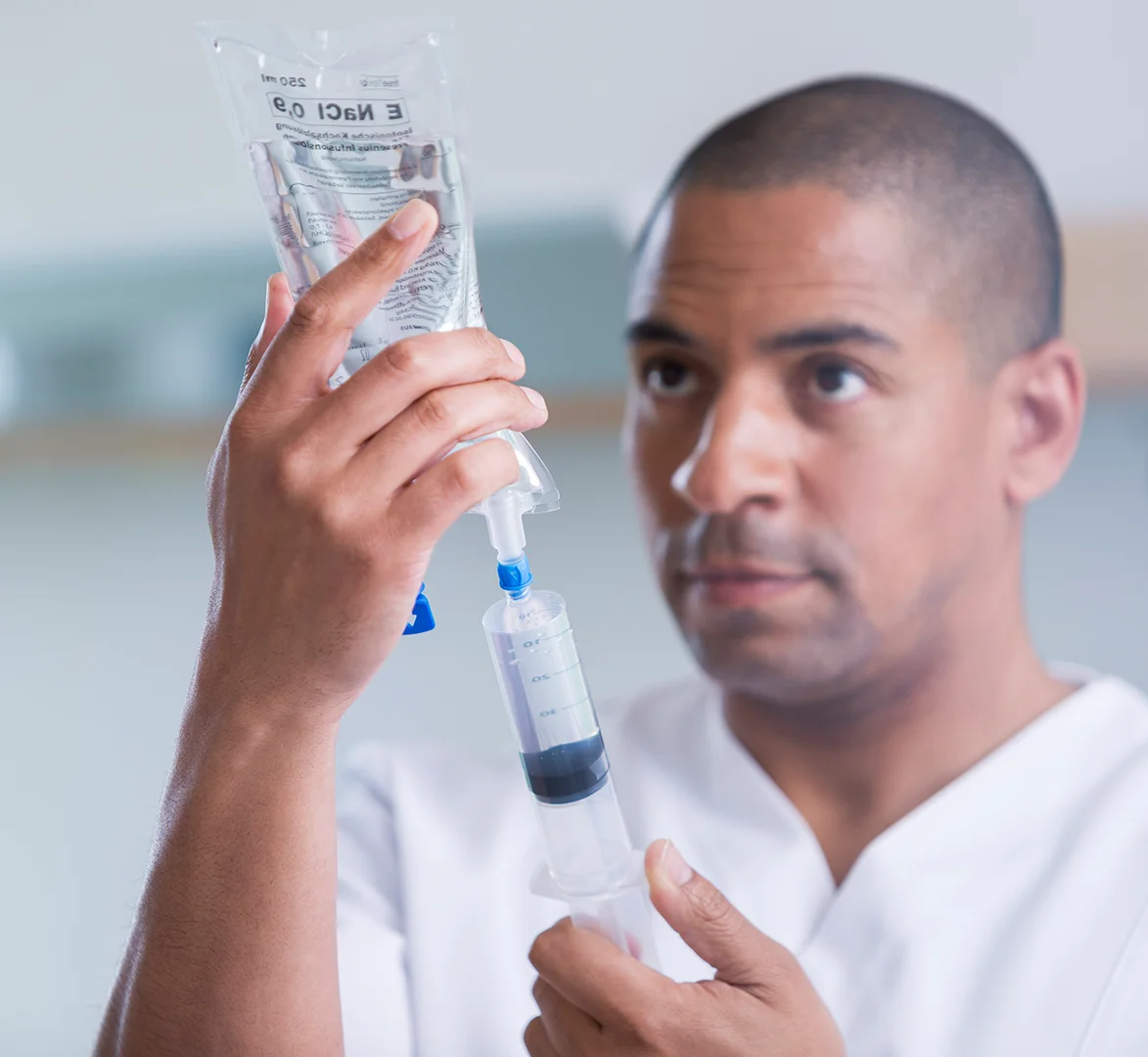 A healthcare worker filling a syringe with a liquid from a medical bag