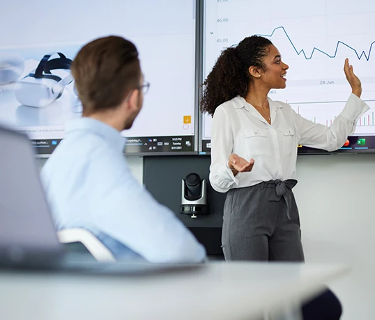 A woman is standing in front of a screen presenting a graph to others