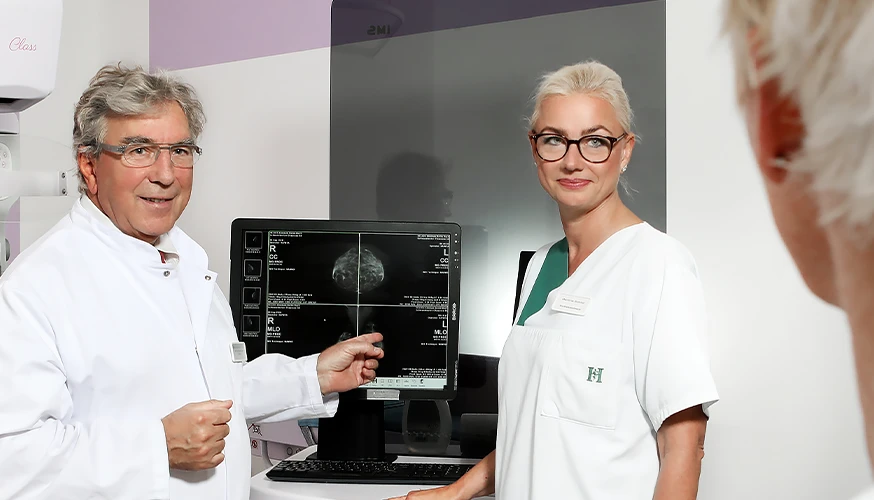Two healthcare workers show a ultrasonic examination to a patient. The patient is barely visible in the picture