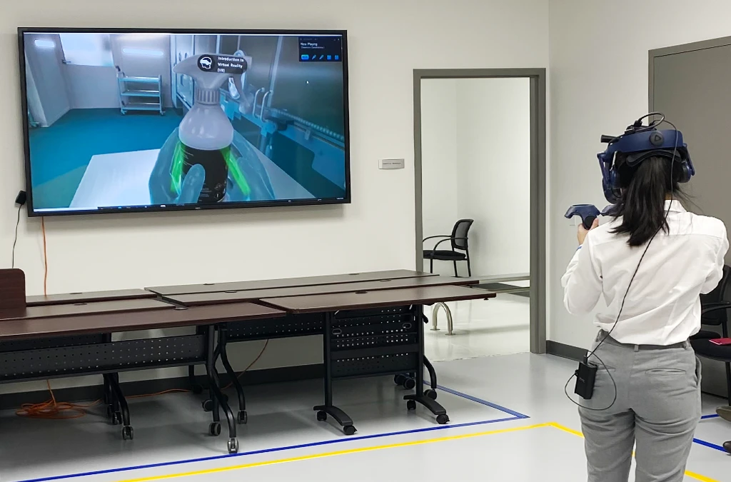 The image shows a person doing an VR simulation, which can be seen on a big screen.
