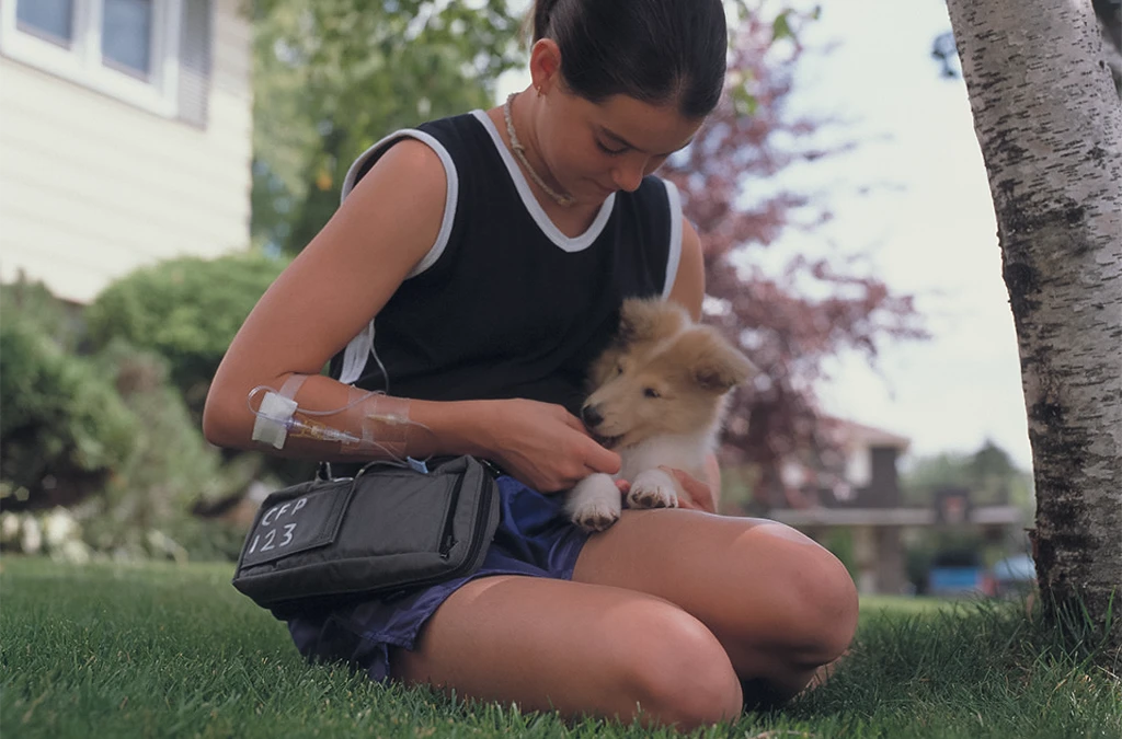 This is an image of a girl kneeling on the grass and petting a small brown dog.